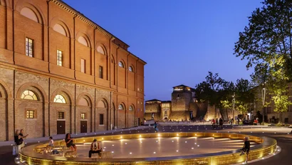 Piazza con illuminazione circolare e persone vicino a un edificio storico di sera