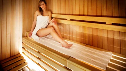 Donna seduta in sauna avvolta in un asciugamano bianco