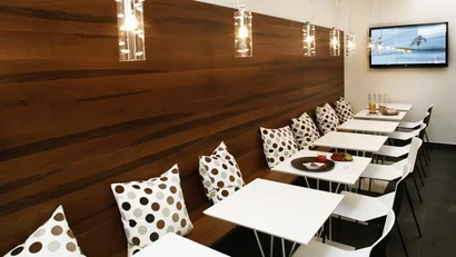 Sala da pranzo moderna con tavoli bianchi, cuscini a pois e TV al muro