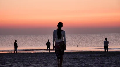 Persone sulla spiaggia al tramonto con cielo arancione e mare calmo