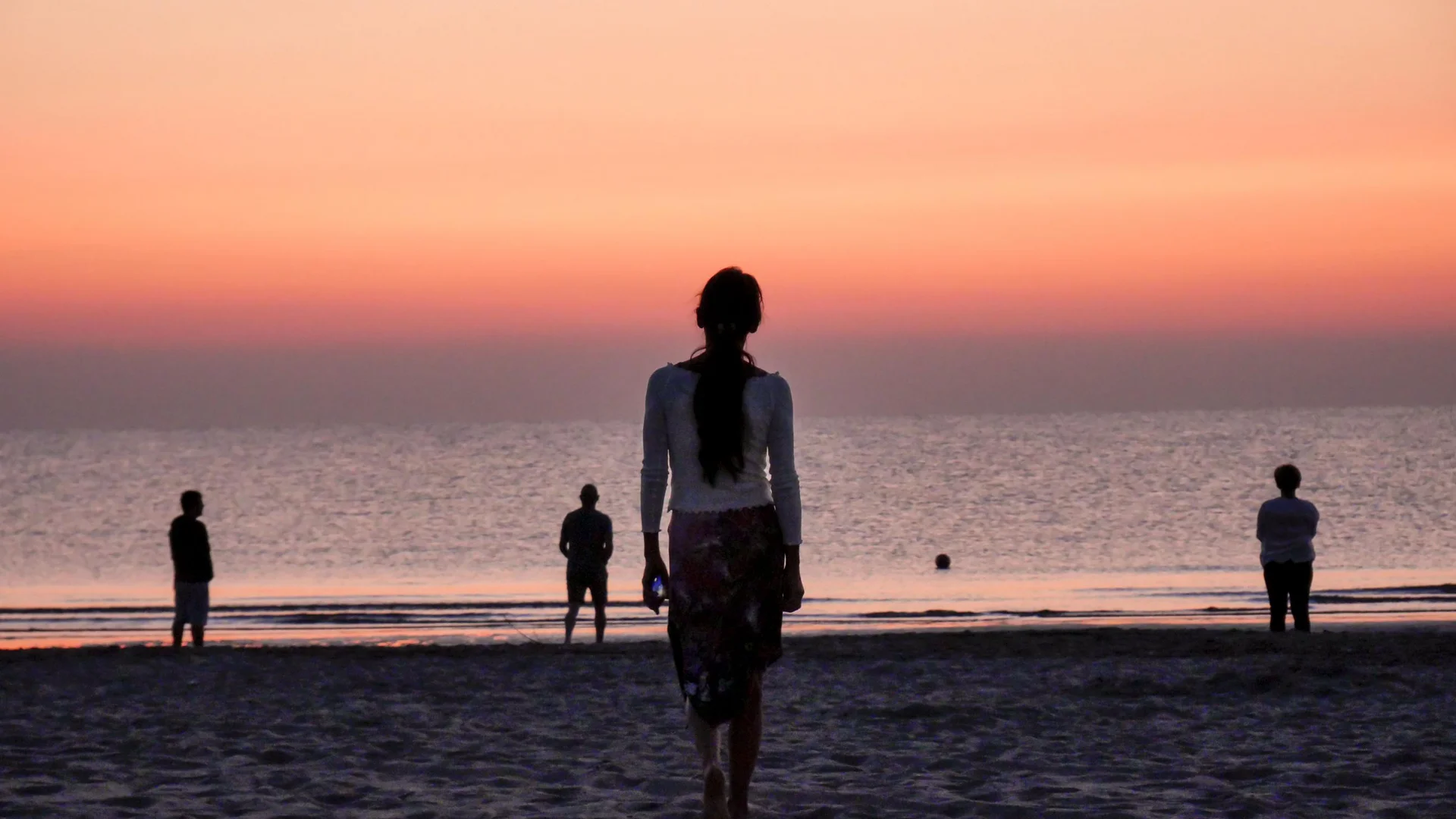 Persone sulla spiaggia al tramonto con cielo arancione e mare calmo